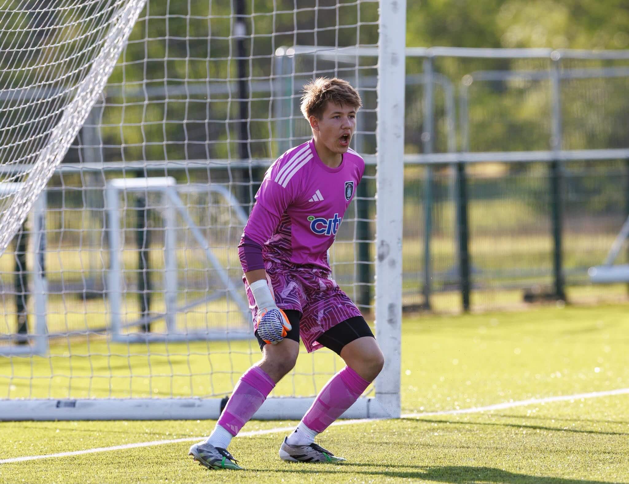 Young football goalkeeper in a pink kit on the pitch. Professional sports physiotherapy Glasgow helps prevent injuries on the field.
